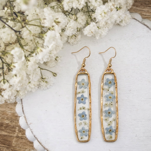 Gold earrings with floral design on a white surface with flowers in the background